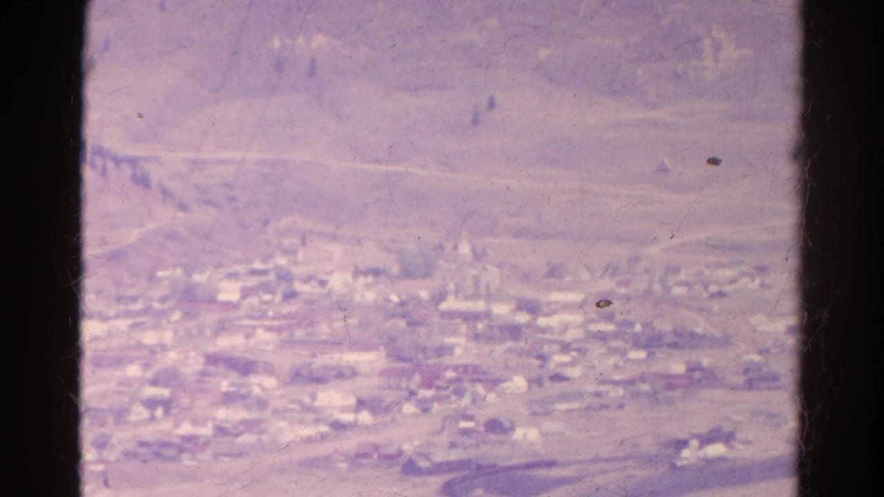 Soft distant view of clustered buildings in a valley with hills and a dark central divider.