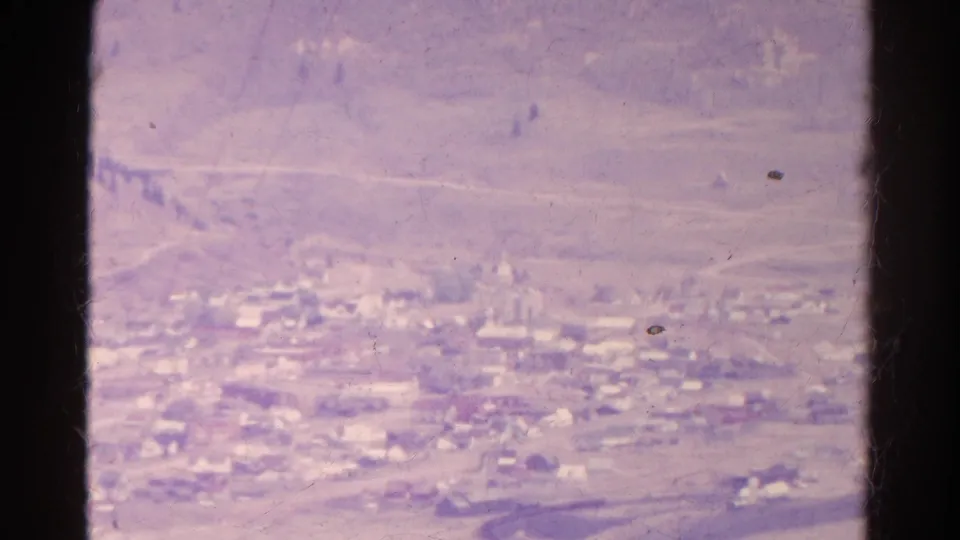 1967 Colorado valley town view with clustered buildings, open hills, and a dark window or viewfinder divider crossing the frame.