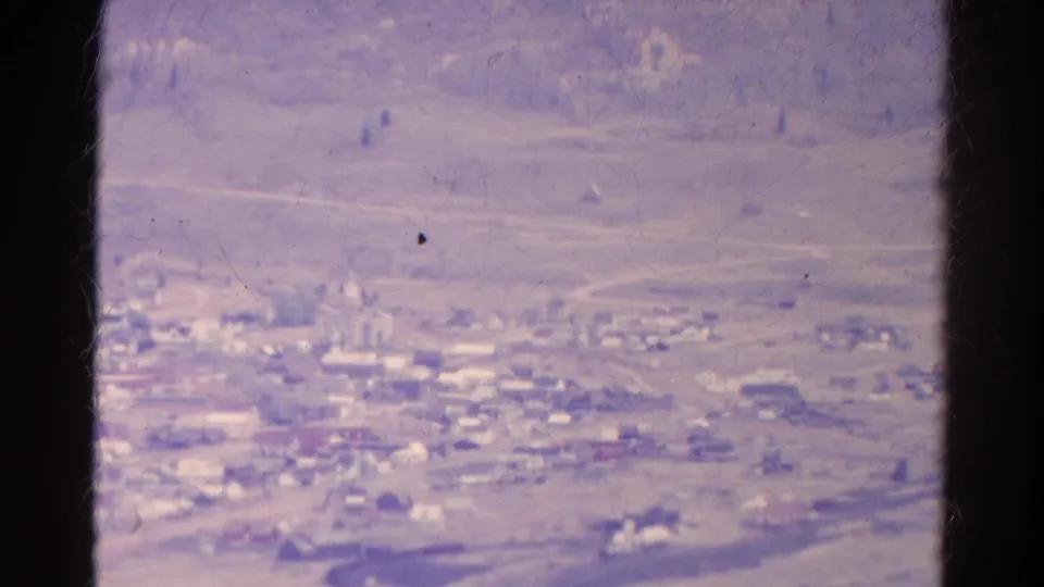Distant 1967 Colorado home-movie view of a valley settlement, pale roads, low buildings, and dark framing edges.