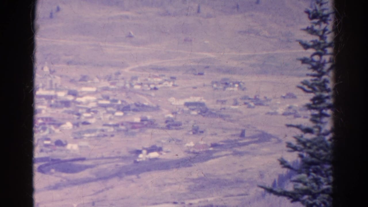 Distant small town below dry hills, framed by dark film edges and an evergreen tree.