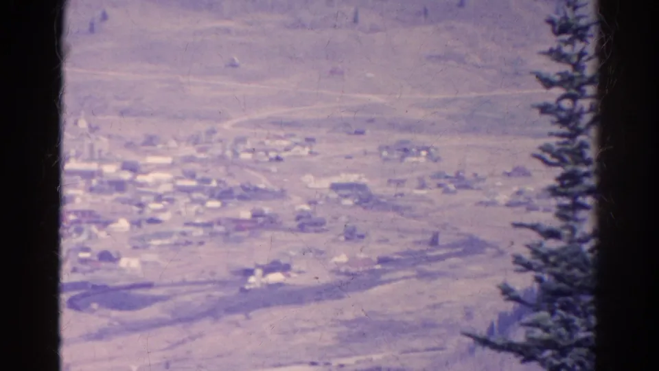 1967 Colorado 8mm frame showing a distant small town across a dry valley, with an evergreen tree along the right edge.