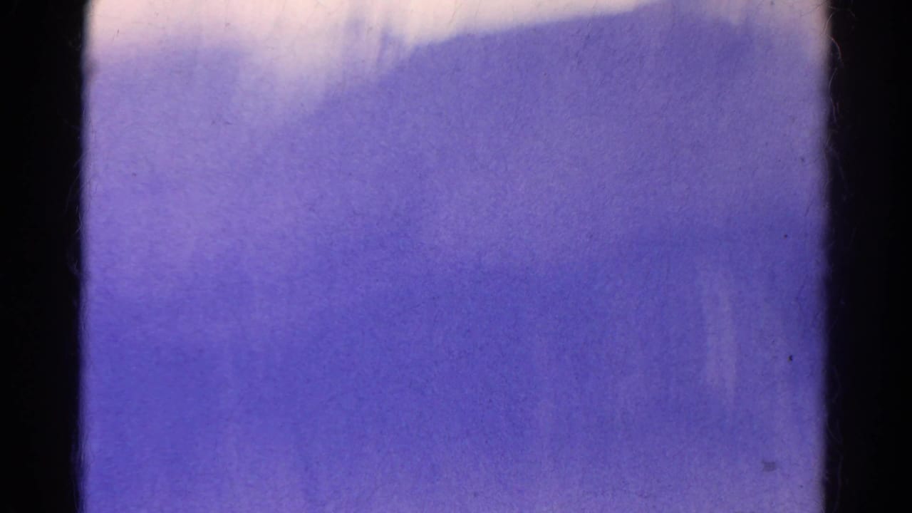 Mostly purple-tinted blurred frame with dark vertical film edges and little landscape detail.
