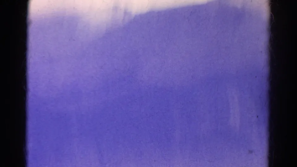 Abstract 8mm frame from the Colorado mountain clip, dominated by purple blur, soft exposure, and dark vertical gate edges.