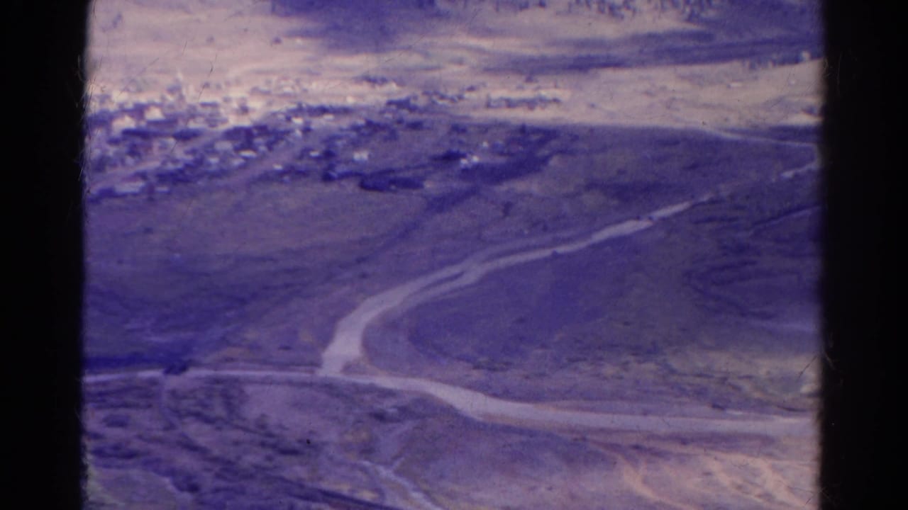 Aerial view of a dry landscape with a winding pale road and small settlement near the upper left.