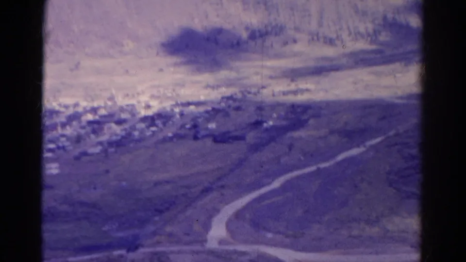 Faded 1967 Colorado 8mm aerial view showing a small settlement, dry terrain, and a curving road across the valley.