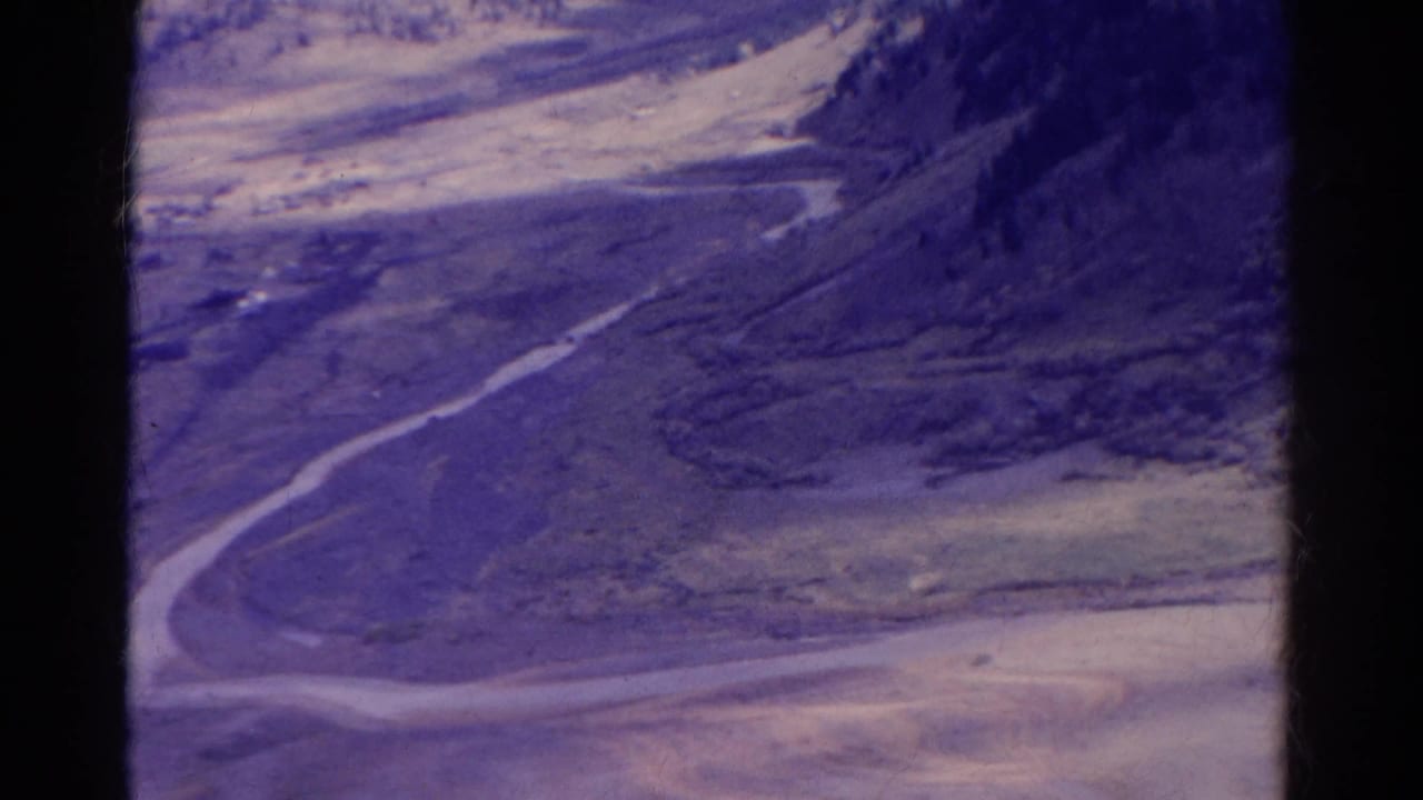 1967 Colorado 8mm view of a mountain valley with a road, soft focus, and purple color shift.
