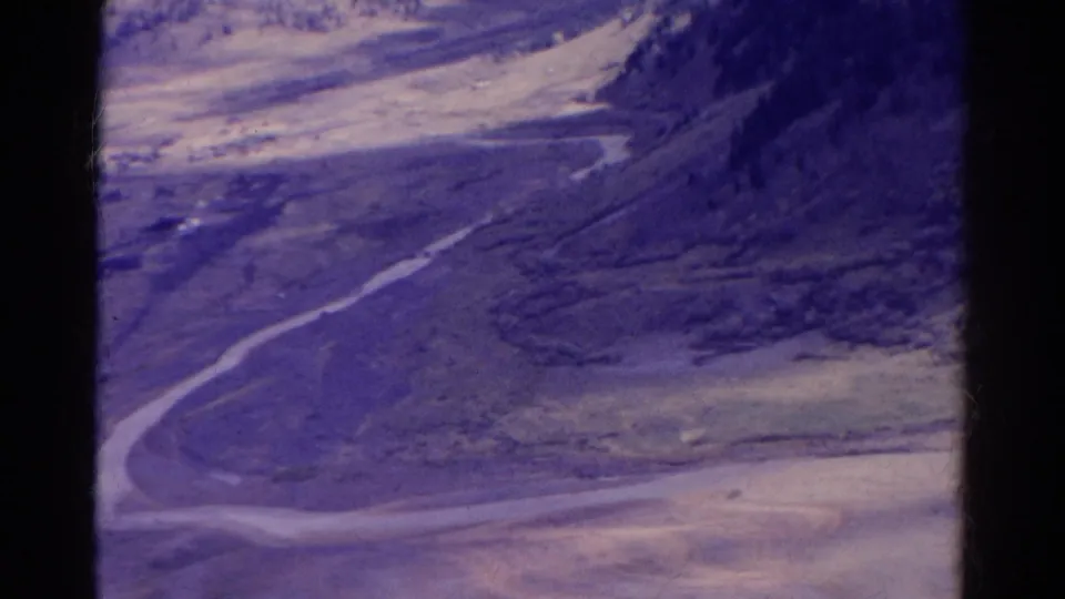 1967 Colorado 8mm view of a mountain valley with a road, soft focus, and purple color shift.