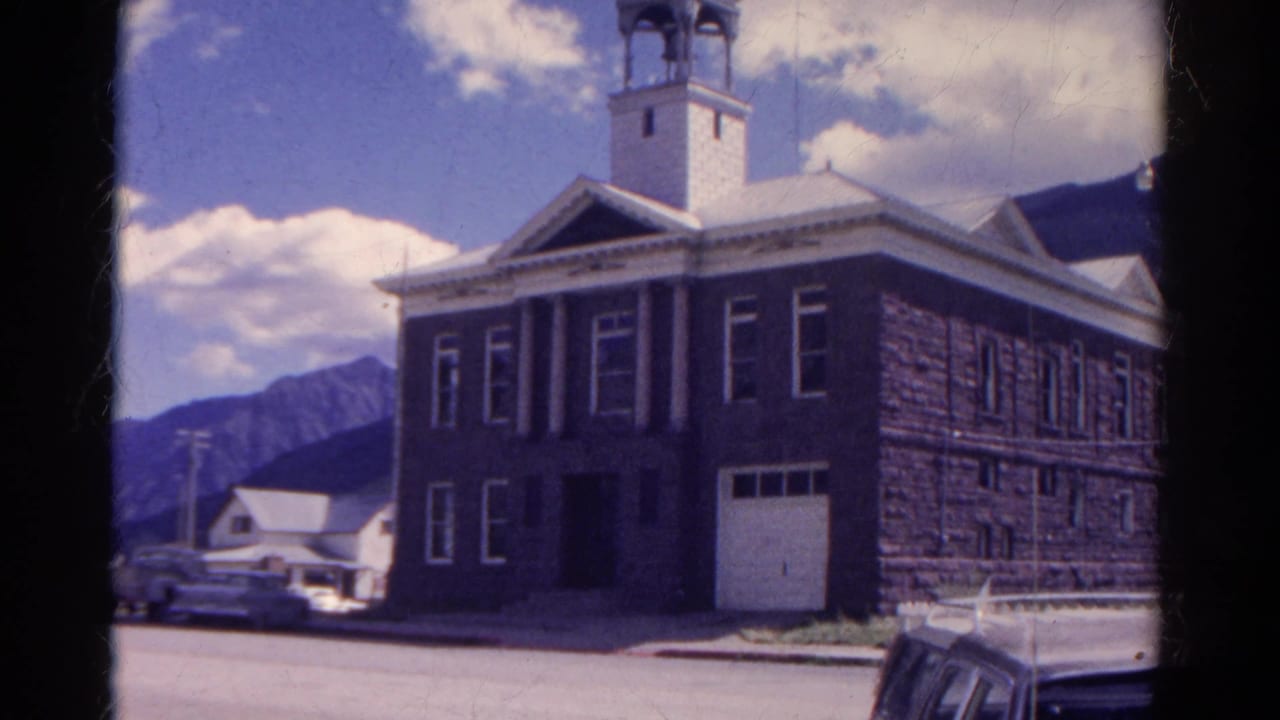 1967 Colorado 8mm frame showing a large stone building with a bell tower, parked cars, and mountains in the background.