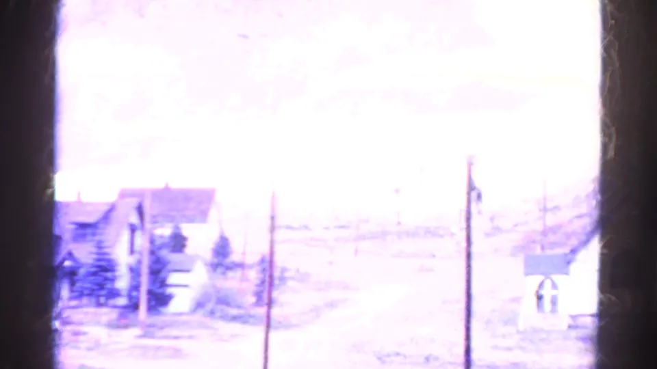 Overexposed 1967 Colorado 8mm frame showing a street edge, small buildings, utility poles, and a bright mountain-town landscape.