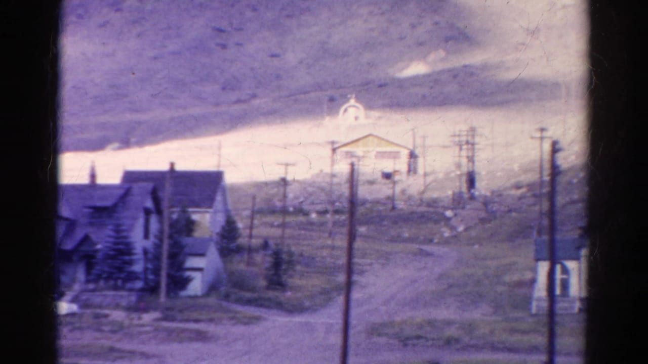 Dirt road passing houses, utility poles, and a small church on a hillside.