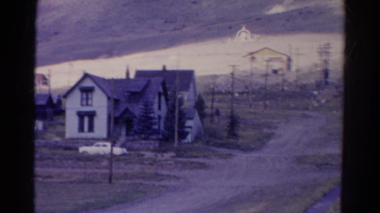 White two-story house beside a dirt road with a parked white car nearby.