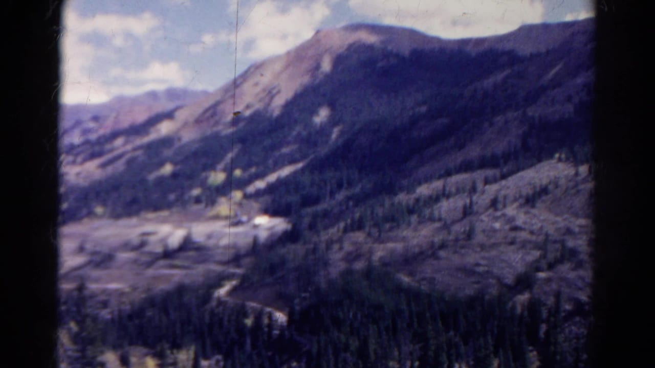 Mountain ridge above a forested valley with bright clouds and dark film edges.