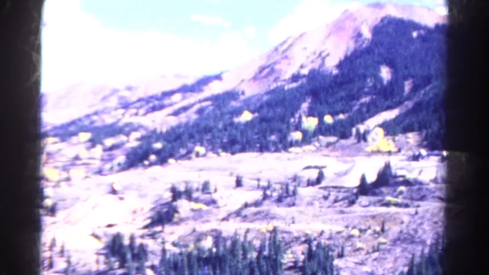 1967 Colorado 8mm frame showing a soft, bright mountain valley view with trees, roads, and cleared mining or industrial terrain.