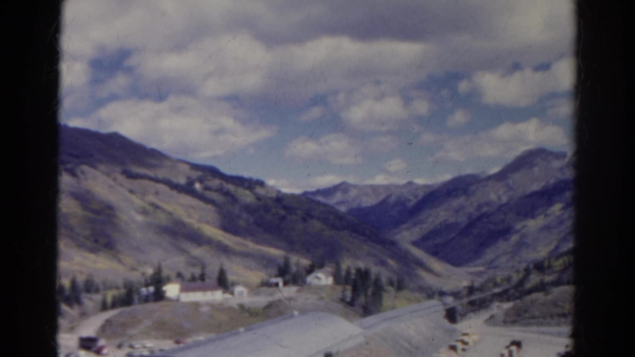 Mountain valley with quarry buildings below a partly cloudy sky.