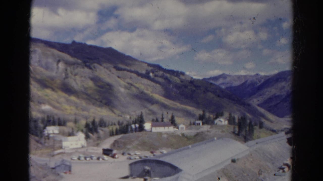 Quarry site with buildings, parked vehicles, and mountains beyond.