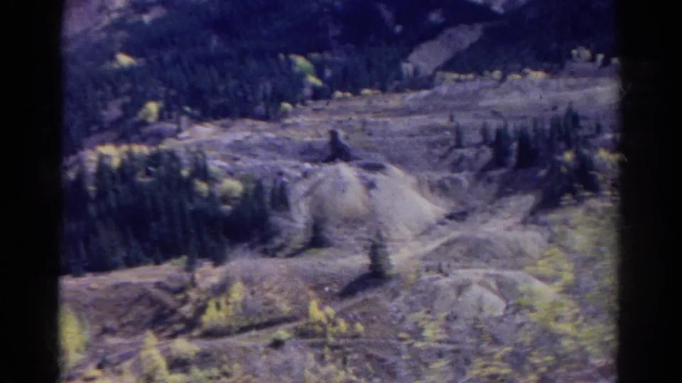 1967 Colorado 8mm frame showing an excavated quarry area with a tunnel-like opening, earth piles, trees, and dark mountain slopes beyond.
