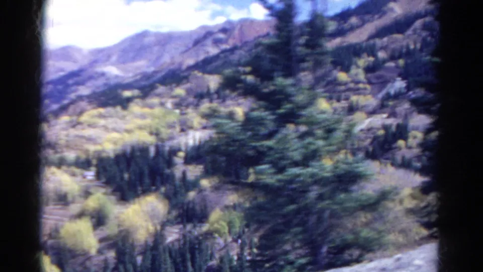 1967 Colorado 8mm driving frame with a blurred evergreen foreground and layered mountain terrain behind it.