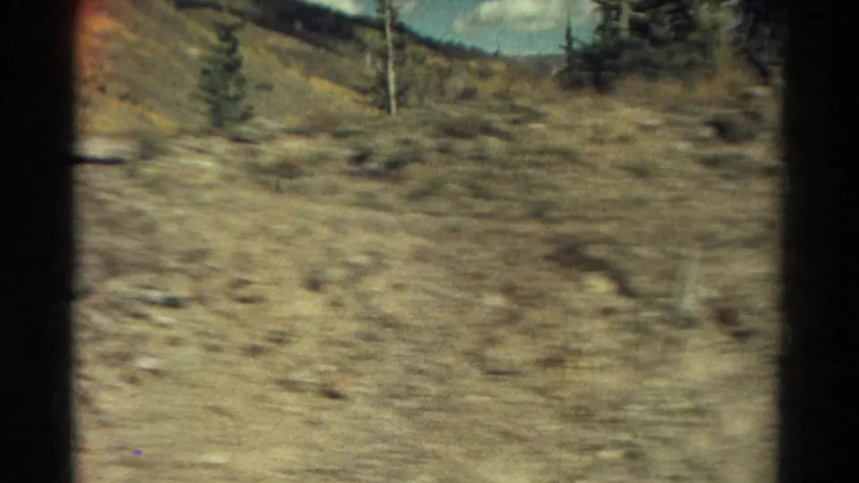 1967 Colorado 8mm frame looking across rocky mountain terrain with scattered evergreens and soft motion blur.