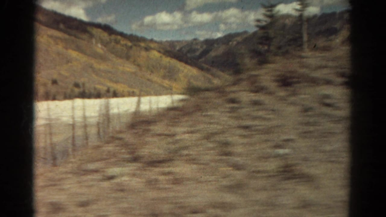 Mountain valley slope with evergreens and a bright horizontal strip in the distance.