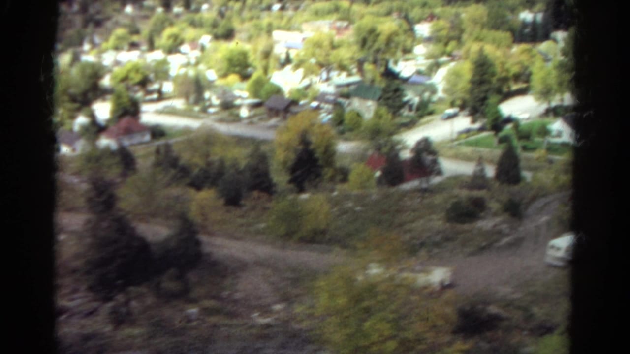 Soft 8mm frame looking down at roads, houses, trees, and a wooded hillside.