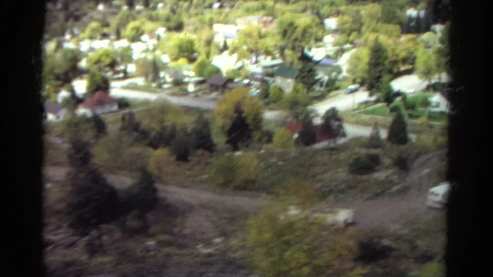 1967 Colorado 8mm view from above a small valley town with light roads, scattered houses, trees, and dark film gate edges.