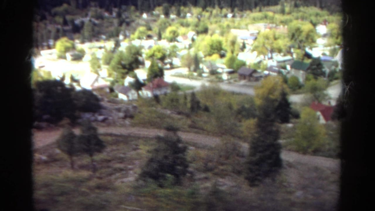 Small town and hillside road seen from above, with houses, trees, and a dark vertical film edge.