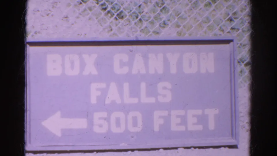 1967 Colorado 8mm frame showing a faded Box Canyon Falls 500 Feet sign mounted below chain-link fencing.