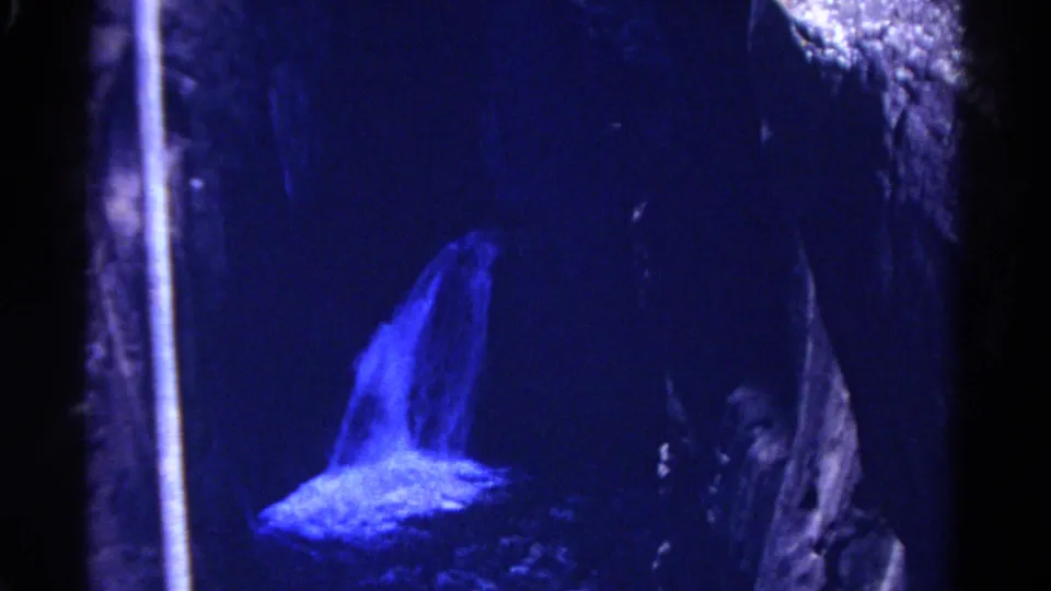 1967 Colorado 8mm frame of a waterfall glowing blue as it drops into a dark rock opening or cavern.