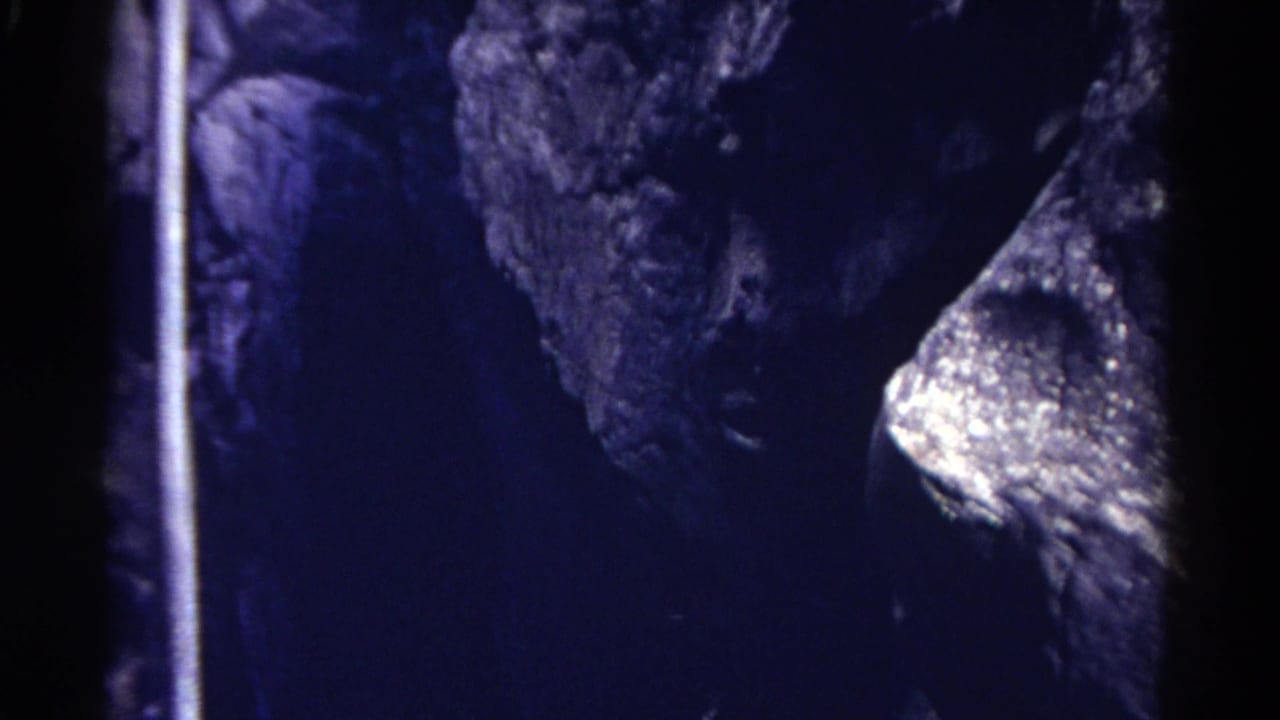 Dark cave wall with blue cast, rough rock, and a bright wet-looking formation.