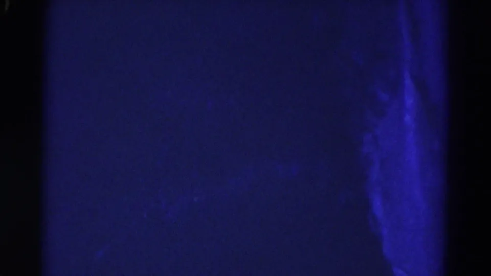 1967 Colorado 8mm frame showing a dim blue cave wall, dark central area, and brighter vertical rock or wet surface at the right edge.