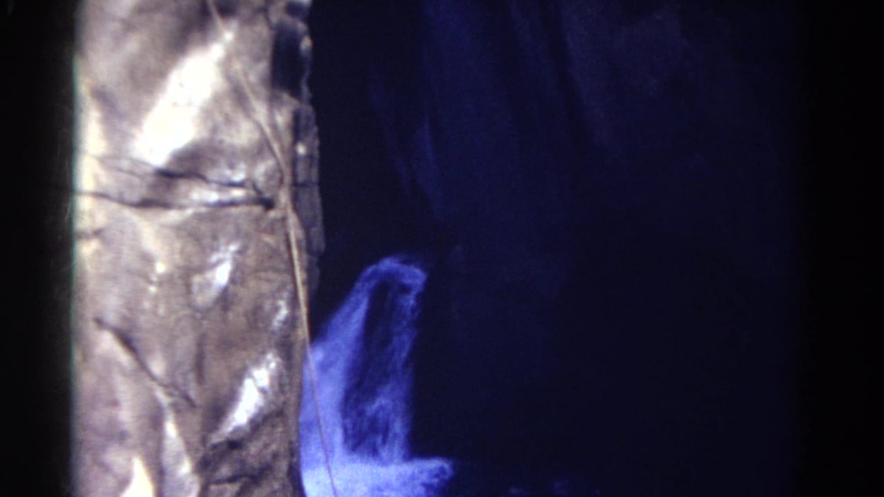 1967 Colorado 8mm frame showing blue-lit water or mist beside a reflective metallic-looking tower in a dark rock-lined space.