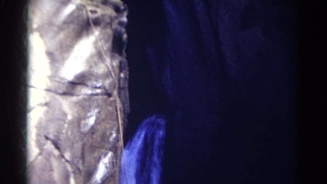 1967 Colorado 8mm frame with a metallic textured tower at left and blue-lit water spray emerging beside it in a dim cave-like area.