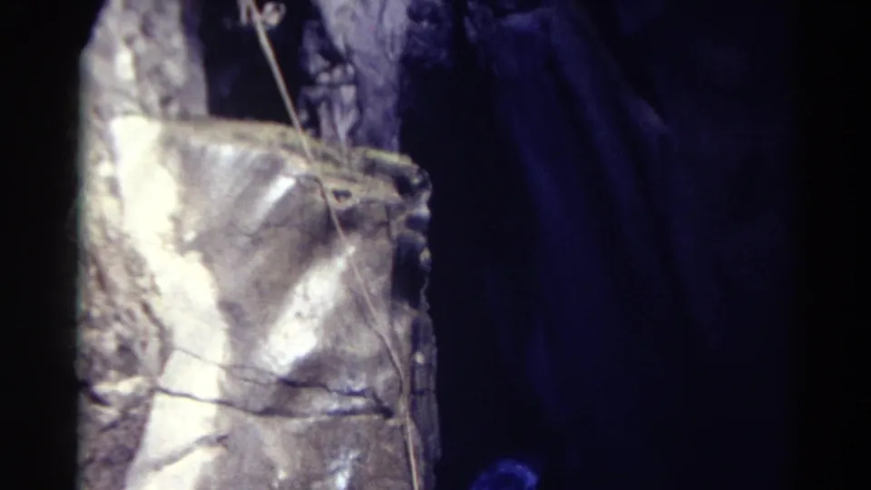 1967 Colorado 8mm frame showing the lower portion of a reflective tower, a dangling rope, and blue illumination in a dark cave-like setting.