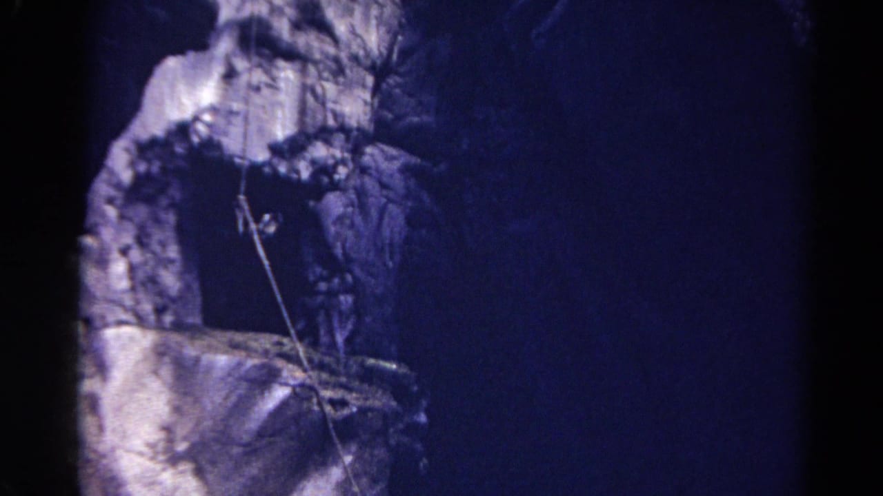 Dark canyon wall seen from below with a rope hanging against rough rock.