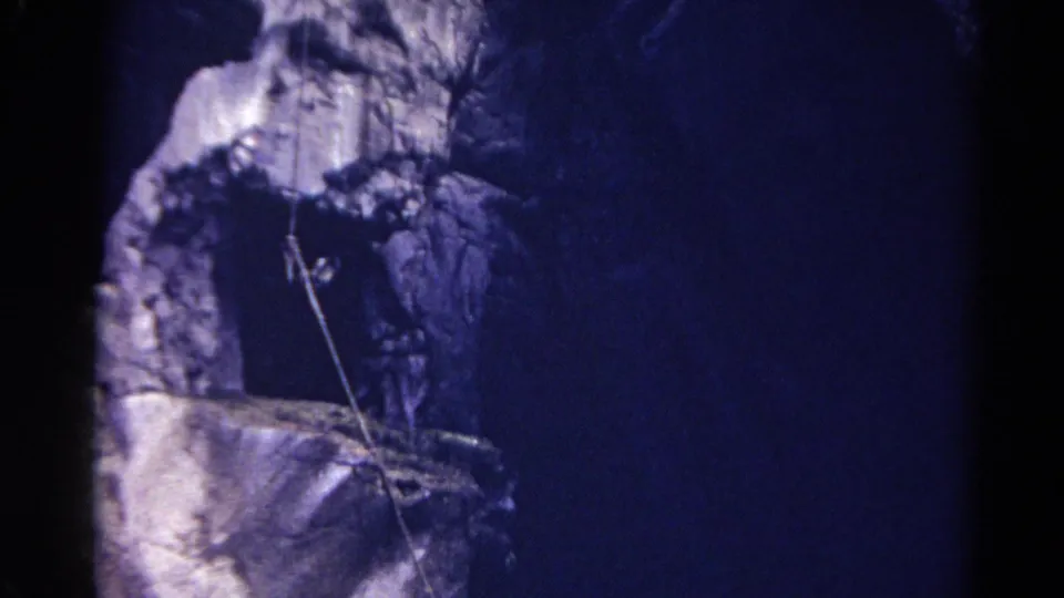 1967 Colorado 8mm frame looking upward at a shadowed rock wall with a rope crossing the stone face.