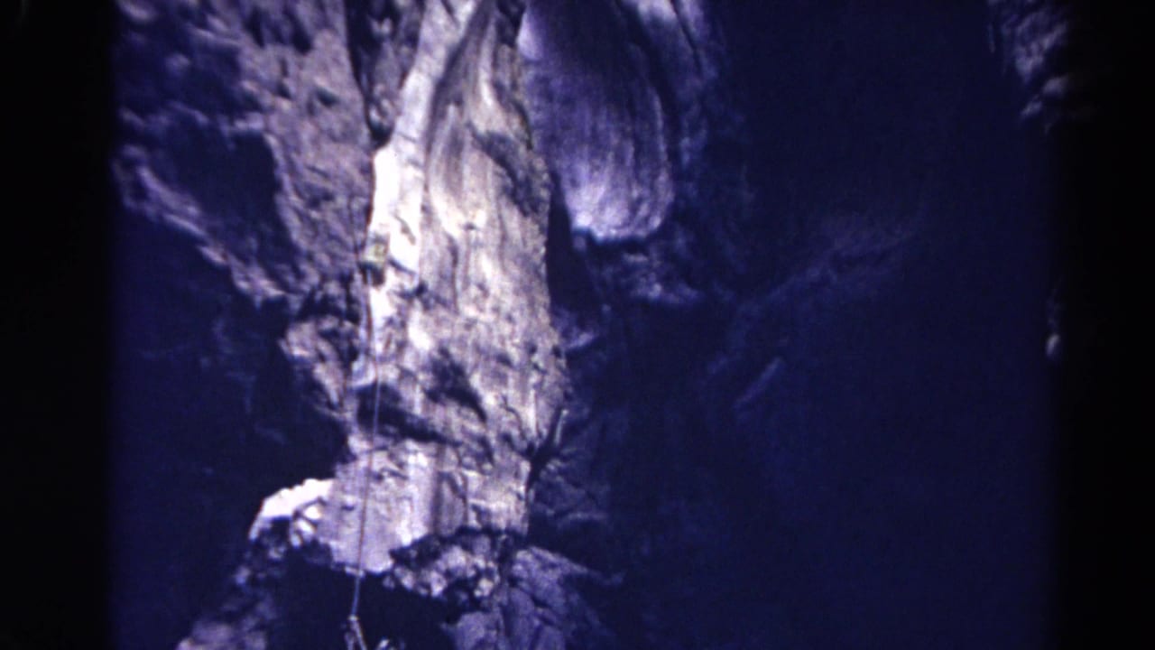 Steep rock face with a rope descending near a bright patch of stone.