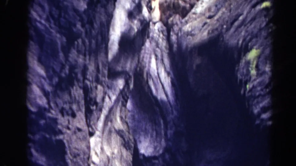 Handheld 1967 Colorado frame looking up through a narrow rocky gap with shadowed stone and sparse vegetation.