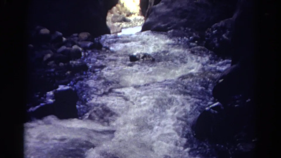 A rocky streambed runs through dark canyon walls toward a bright sunlit opening in Colorado.