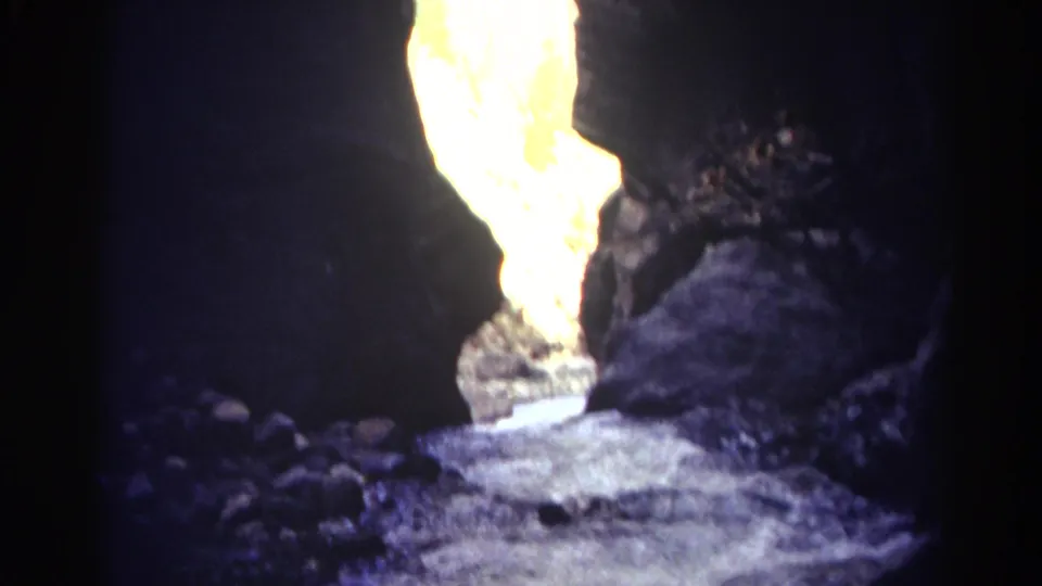 A bright slit of sunlight frames rock walls above a shadowed stream in 1967 Colorado canyon footage.