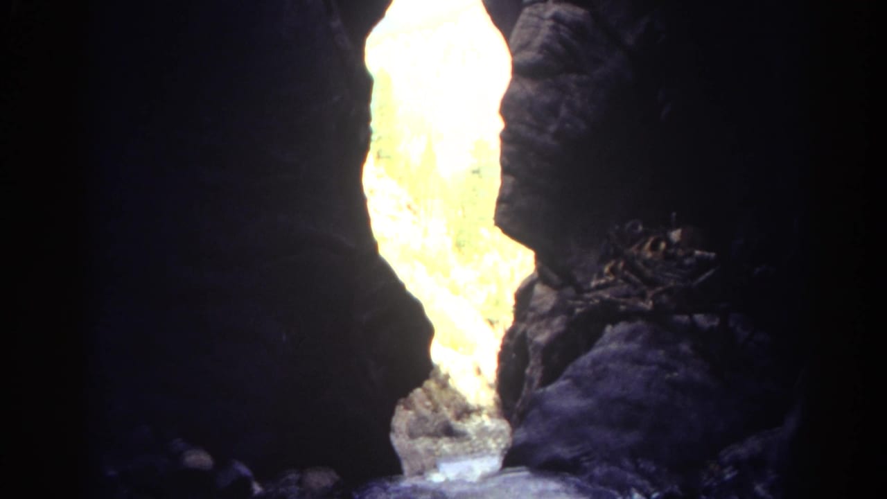 Dark canyon walls frame a bright sunlit rock opening with a hint of water below.