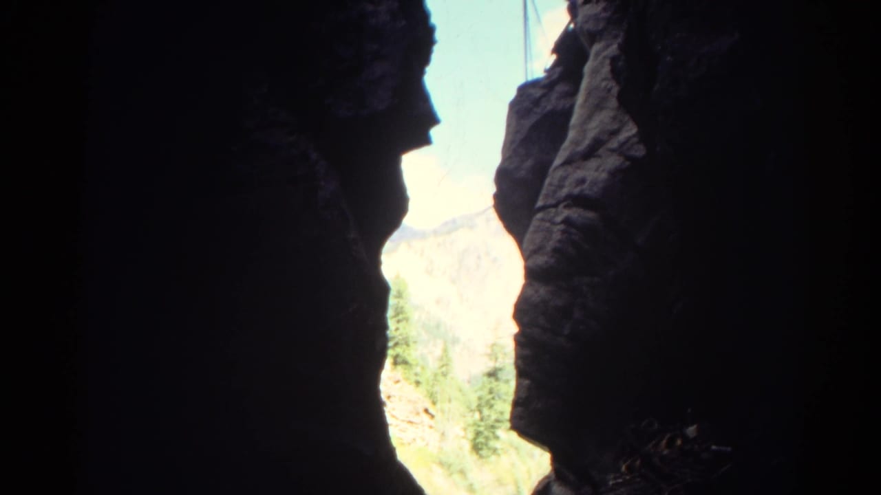 1967 Colorado home-movie view from inside a canyon, with dark rock edges around sunlit mountains and vegetation.