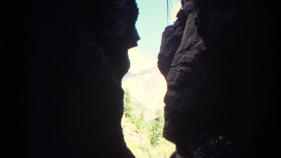 1967 Colorado home-movie view from inside a canyon, with dark rock edges around sunlit mountains and vegetation.