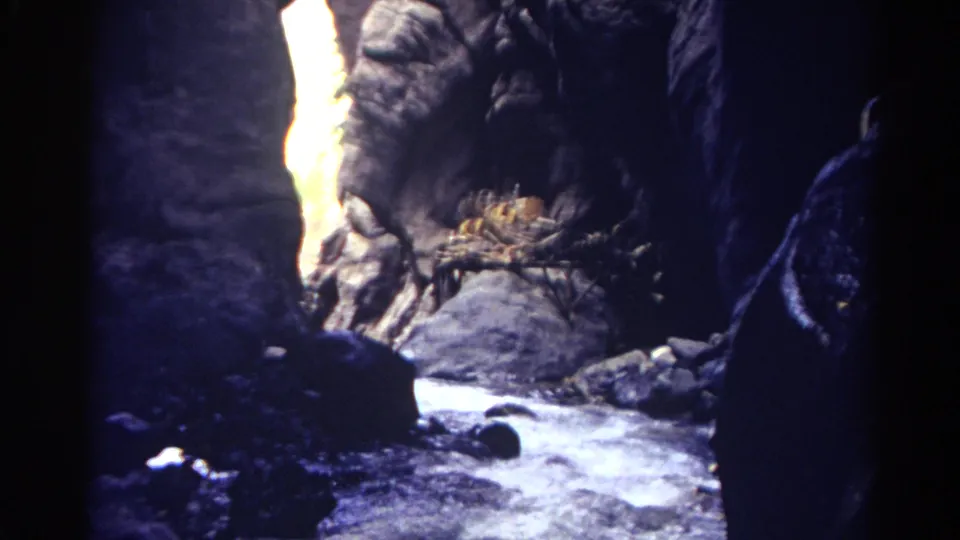 1967 Colorado 8mm frame of bright water moving between shadowed rock walls and boulders in a narrow canyon.