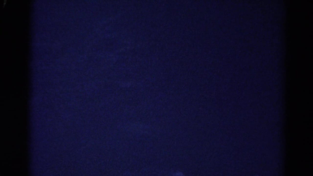 1967 Colorado 8mm frame looking into a very dark cave interior with blue cast, grain, and indistinct rock surfaces.