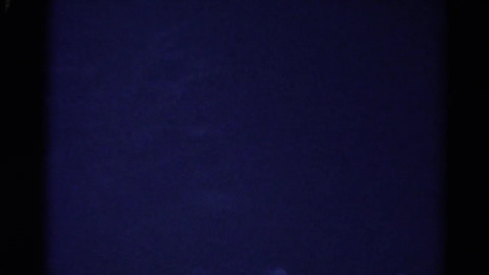 1967 Colorado 8mm frame looking into a very dark cave interior with blue cast, grain, and indistinct rock surfaces.