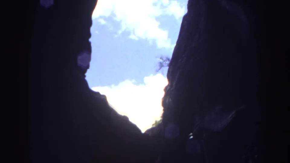 1967 Colorado 8mm frame from inside a cave, with dark rock silhouettes framing blue sky and pale clouds outside.
