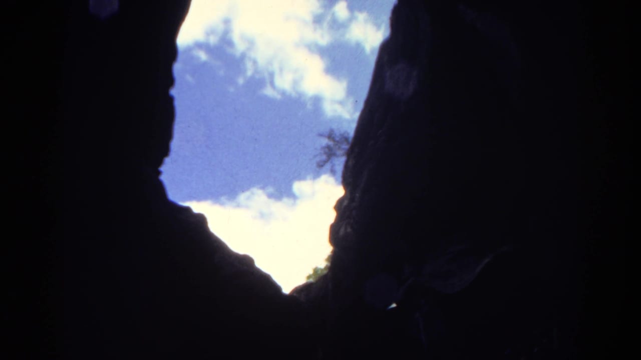 1967 Colorado 8mm frame looking from a dark rock opening toward bright sky and clouds, with cave walls in deep shadow.