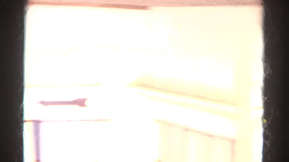 Overexposed transitional frame, likely near a window or bright surface, with dark edges and washed yellow-white light.