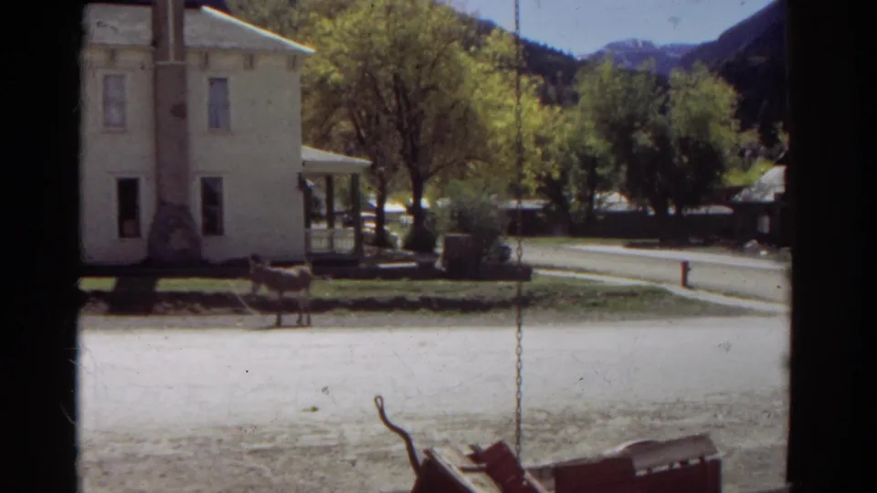 1967 Colorado frame showing a horse near a white house, a swing chain in the foreground, and trees and mountains beyond the road.