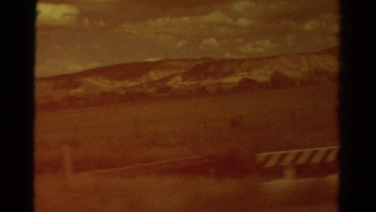 Faded 8mm frame from rural Colorado showing open ground, distant low hills, cloudy sky, and a striped object near the right edge.